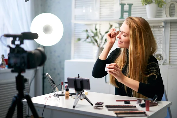 Beauty blogger woman filming daily make-up routine tutorial at camera on tripod. Influencer girl live streaming cosmetics product review in home studio. Vlogger female applies skin powder with brush. — Stock Photo, Image