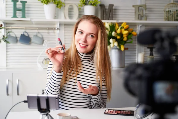 Vlogger female showing lipstick. Beauty blogger woman filming daily make-up routine tutorial near camera on tripod. Influencer blonde girl live streaming cosmetics product review in home studio — Stock Photo, Image