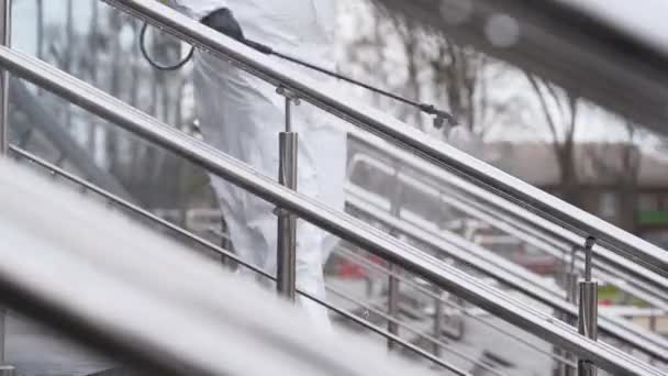 Sanitizer desinfecteert railing touch oppervlakken op coronavirus covid-19 quarantaine met antibacteriële sproeier. Werknemer in gasmasker en hazmat beschermend pak reinigt leuningen in de stad openbare plaats. — Stockvideo
