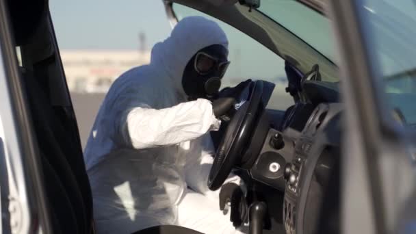 El trabajador del equipo de materiales peligrosos desinfecta el volante con una toallita desinfectante antibacteriana en la cuarentena del covid-19 del coronavirus. Hombre con máscara de gas, traje hazmat limpia el interior del coche con trapo y lavadora pulverizadora . — Vídeo de stock