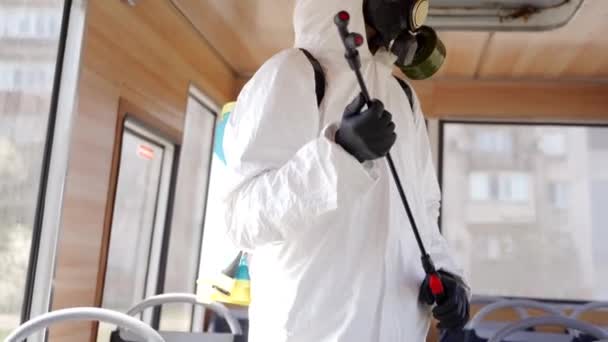 バス内のコロナウイルスcovid-19隔離上の抗菌消毒剤噴霧器でハズマットチームの労働者の英雄的なショット。ガスマスクの男は、洗濯機で公共交通機関のインテリアを消毒し、カメラを見て. — ストック動画