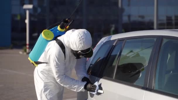 Hazmat team worker disinfects car door handles with antibacterial sanitizer wipe on coronavirus covid-19 quarantine. Man in gas mask, hazmat suit cleans parked car body with rag and sprayer washer. — Stock Video
