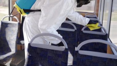 Tehlikeli madde ekibi çalışanı otobüsün içini antibakteriyel dezenfektanla dezenfekte ediyor. Coronavirüs covid-19 karantinasında. Gaz maskeli adam, tehlikeli madde giysisi toplu taşıma koltuklarını temizliyor, bez parçasıyla tutunuyor..