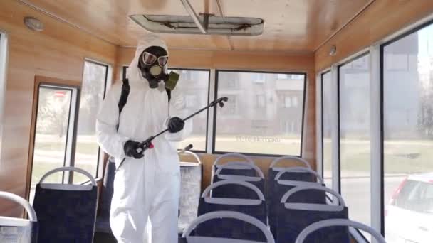 Hazmat team worker disinfects bus seats with antibacterial sanitizer sprayer on coronavirus covid-19 quarantine. Man in gas mask, hazmat suit cleans public transport interior, handholds with washer. — Stock Video