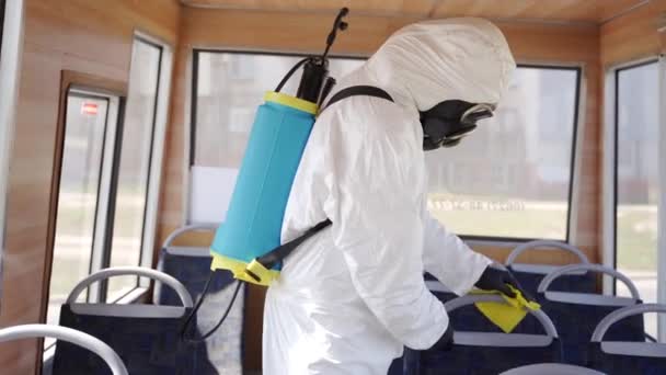 Hazmatチームの労働者はコロナウイルスのcovid-19隔離の抗菌消毒剤でバスの内部を消毒します。ガスマスクの男、ハズマットスーツは公共交通機関の座席をきれいにし、ラグで手を取ります。ヒーローショット. — ストック動画