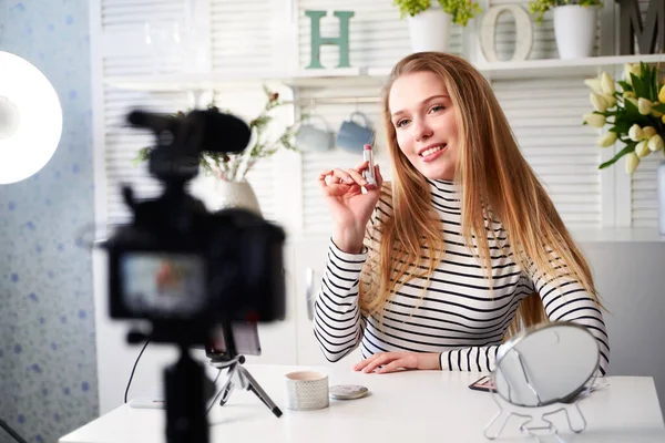 Vlogger kvinna visar läppstift. Skönhetsbloggare kvinna filmar dagliga make-up rutin handledning nära kameran på stativ. Influencer blond flicka live streaming kosmetika produktrecension i hemstudio — Stockfoto