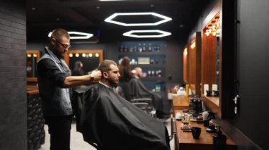 Son moda berber berber dükkanında sakallı adamın saçını kırpıcı ile kesiyor. Kuaförde erkek saç kesimi ve saç kesimi. Saçını budayarak mı? Kuaför retro kuaförde saç kesimi yapıyor. İzleme