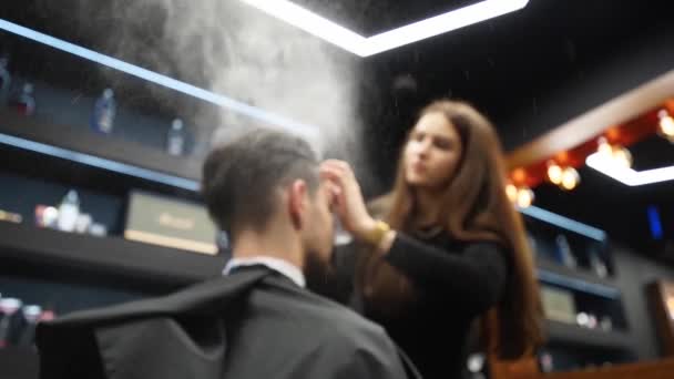 Парикмахер брызгает воду на волосы клиента перед стрижкой и укладкой в парикмахерской. Парикмахерша мочит волосы спреем и расчесывает их в парикмахерской. Мастер использует бутылку из-под воды в мужской косметической студии . — стоковое видео