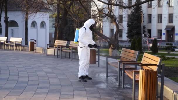 Ο εργάτης της ομάδας Hazmat απολυμαίνει πάγκους με αντιβακτηριδιακό ψεκαστήρα σε καραντίνα του Coronavirus covid-19. Man in gas mask, hazmat suit καθαρίζει δημόσια εγκατασταθούν καρέκλες στο πάρκο με πλυντήριο πίεσης. — Αρχείο Βίντεο