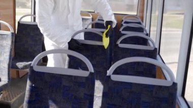 Tehlikeli madde ekibi çalışanı otobüsün içini antibakteriyel dezenfektanla dezenfekte ediyor. Coronavirüs covid-19 karantinasında. Gaz maskeli adam, tehlikeli madde giysisi toplu taşıma koltuklarını temizliyor, bez parçasıyla tutunuyor..