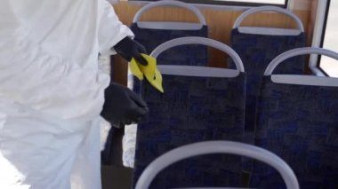Tehlikeli madde ekibi çalışanı otobüsün içini antibakteriyel dezenfektanla dezenfekte ediyor. Coronavirüs covid-19 karantinasında. Gaz maskeli adam, tehlikeli madde giysisi toplu taşıma koltuklarını temizliyor, bez parçasıyla tutunuyor..