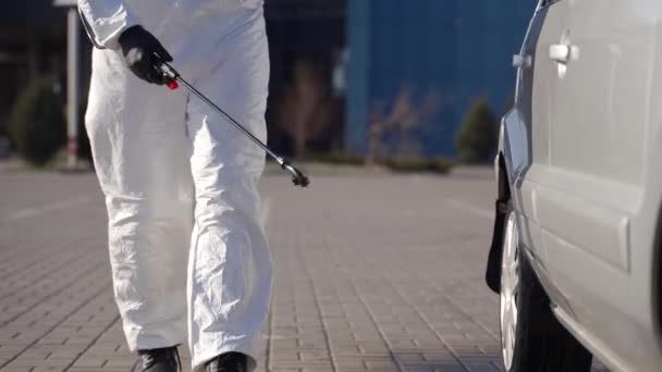 Hazmat team worker disinfects car wheels with antibacterial sanitizer sprayer on coronavirus covid-19 quarantine. Man in gas mask, hazmat suit cleans parked car tires and body with pressure washer. — Stock Video