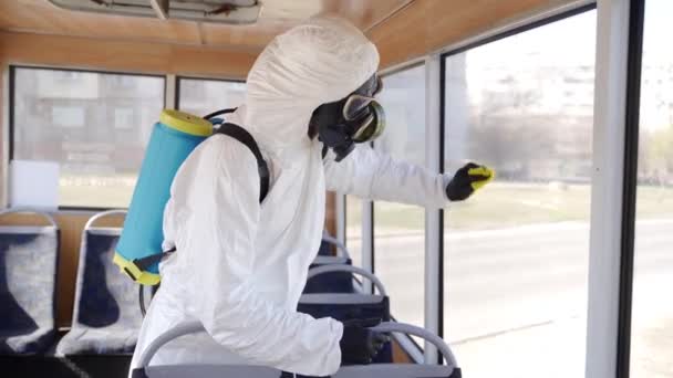 Pracownik zespołu Hazmat dezynfekuje wnętrze autobusu antybakteryjnymi chusteczkami dezynfekującymi w trakcie kwarantanny coronavirus covid-19. Mężczyzna w masce gazowej, kombinezon czyści siedzenia transportu publicznego, uchwyty z szmatą. — Wideo stockowe