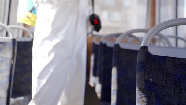 バス内のコロナウイルスcovid-19隔離上の抗菌消毒剤噴霧器でハズマットチームの労働者の英雄的なショット。ガスマスクの男は、洗濯機で公共交通機関のインテリアを消毒し、カメラを見て. — ストック動画