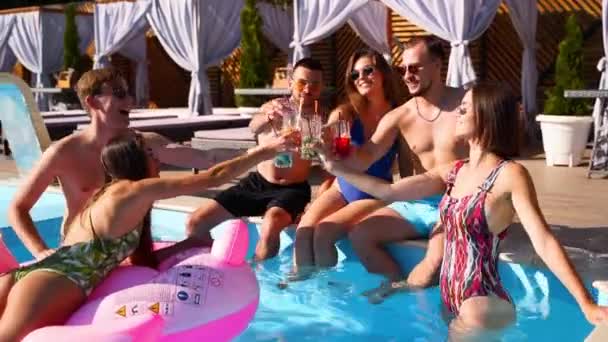 Grupo multirracial de amigos brindando, tintineo vasos con cócteles en la fiesta de la piscina. Jóvenes felices en traje de baño bailando, discotecas con flamenco inflable, colchones en resort de lujo. — Vídeo de stock