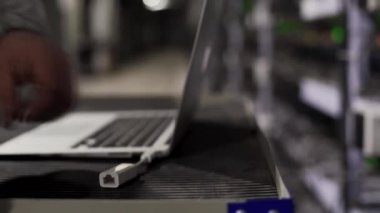 Teknisyen dizüstü bilgisayara ethernet kablo bağlayıcısı yerleştiriyor arka planda dongle soketi ve ağ donanım ışıkları var. Veri merkezi ekipman sunucusu servis odasında. İnternet kablosu ekleyen yönetici.