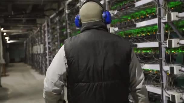 Technik diagnostyki centrum danych spaceruje po stojakach sprzętu górniczego w serwerowni. Administrator sieci sprawdza duży klaster komputerowy ze sprzętem sieciowym. Inżynier serwisu górników ASIC. — Wideo stockowe