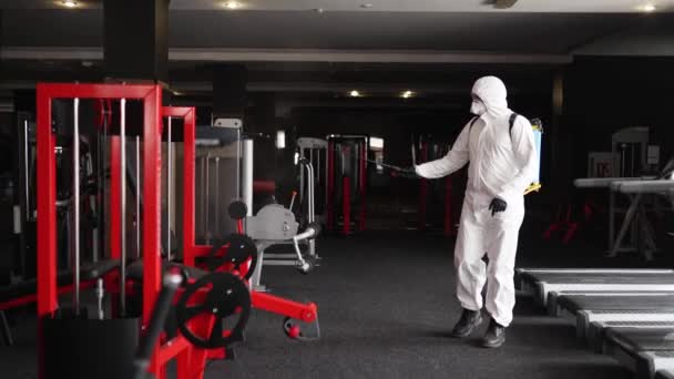 Der Mitarbeiter von Hazmat desinfiziert Fitnessgeräte in Fitnessstudios mit antibakteriellen Desinfektionsspray unter Quarantäne von Coronavirus covid-19 Hazard. Mann im Schutzanzug reinigt Trainingsgerät auf Trainingsplatz. — Stockvideo