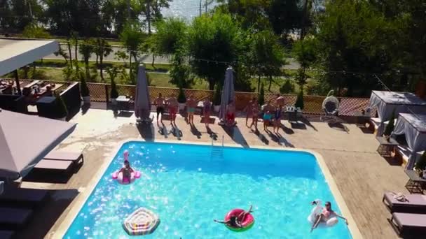 Felices amigos saltando y salpicando en la piscina con flotadores inflables en el complejo de lujo. Jóvenes en traje de baño teniendo fiesta en villa privada de vacaciones. Chicas calientes saltan al agua. Movimiento lento. — Vídeo de stock