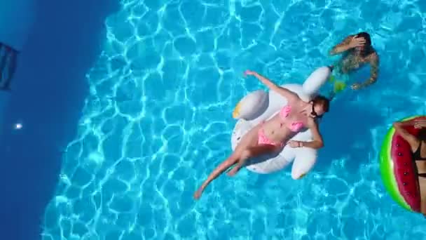 Aérea. Amigos que se enfrían en la piscina con flamenco inflable, cisne, colchón. Los jóvenes felices se bañan en colchones flotantes en un resort de lujo. Vista desde arriba. Chicas en bikini tomando el sol — Vídeos de Stock