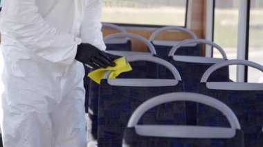 Tehlikeli madde ekibi çalışanı otobüsün içini antibakteriyel dezenfektanla dezenfekte ediyor. Coronavirüs covid-19 karantinasında. Gaz maskeli adam, tehlikeli madde giysisi toplu taşıma koltuklarını temizliyor, bez parçasıyla tutunuyor..