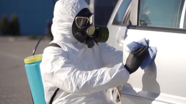 Hazmat team worker disinfects car door handles with antibacterial sanitizer wipe on coronavirus covid-19 quarantine. Man in gas mask, hazmat suit cleans parked car body with rag and sprayer washer. — Stock Video