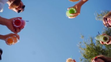 Arkadaşların havuz partisinde eğlenmesi, otel havuzunun yanında renkli yaz kokteylleri içmesi. İnsanlar yaz köşkünde yavaş çekimde taze meyve suyu içerek kadeh kaldırıyorlar..