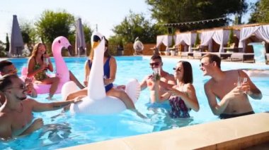 Arkadaşların havuzda kokteyllerle parti veriyor. Mayo dansındaki mutlu gençler, güneşli bir günde şişme flamingo, kuğu ve şilte ile gece kulübü. Yavaş çekim