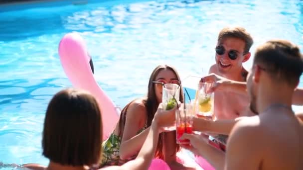 Multiraciale groep vrienden toasten, klinkende glazen met cocktails op een zwembadfeest. Gelukkige jonge mensen in zwemkleding dansen, clubbing met opblaasbare flamingo, matrassen in luxe resort. — Stockvideo