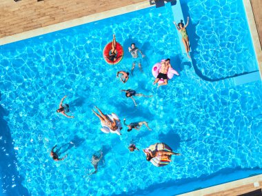 Havuzda, şişme flamingo, kuğu ve şiltelerle parti veren arkadaşlar. Lüks otellerde mutlu genç insanlar drone kameralarına el sallıyor. Yukarıdan bak. Bikinili kızlar güneşleniyor..