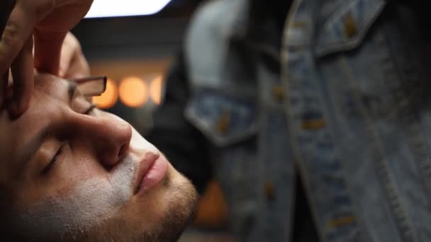 Professional barber shaves customer beard with straight razor. Beard cut with old-fashioned blade at barbershop. Handsome macho man getting his beard shaved in studio. Close-up shot. — Stock Video