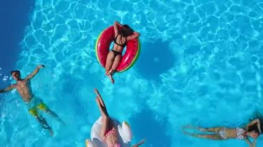 Havadan. Arkadaşlar yüzme havuzunda şişme flamingo, kuğu ve şilte ile takılıyor. Lüks otellerde yüzen yataklarda banyo yapan mutlu gençler. Yukarıdan bak. Bikinili kızlar güneşte güneşleniyor.