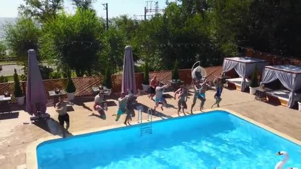 Glada vänner hoppar och stänk i poolen med uppblåsbara flöten i lyx resort. Ungdomar i badkläder har fest i privat semestervilla. Heta tjejer hoppar i vatten. Långsamma rörelser. — Stockvideo