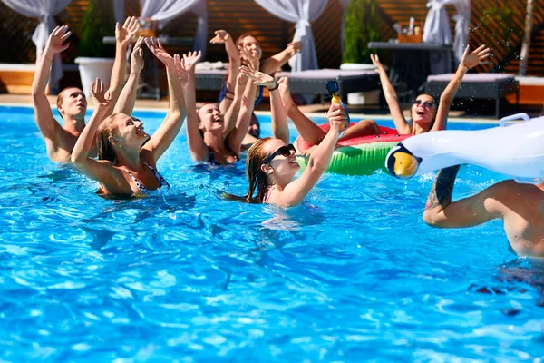 Grupo multirracial de amigos que fazem festa na piscina villa privada. Jovens felizes em roupa de banho dançando e salpicando com flutuações infláveis no resort de luxo no dia ensolarado. Meninas de biquíni. — Fotografia de Stock