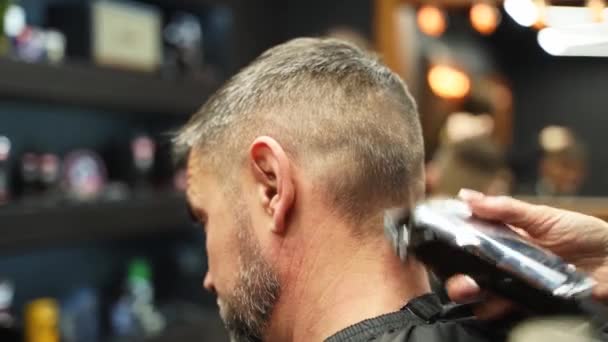 Barber woman cuts bearded mans hair with a clipper in barbershop. Mens hairstyling and hair cutting in salon. Grooming the hair with trimmer. Hairdresser doing haircut in retro hair salon. — Stock Video