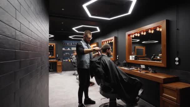 El peluquero moderno corta el cabello de los hombres barbudos con un cortador en la barbería. Para hombre peinado y corte de pelo en el salón. Aseo el cabello con trimmer. Peluquería haciendo corte de pelo en peluquería retro. Dolly en — Vídeos de Stock