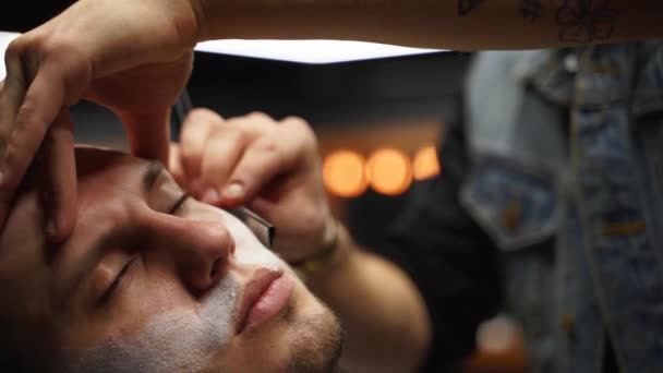 Peluquero profesional afeita la barba del cliente con navaja de afeitar. Barba cortada con hoja pasada de moda en la peluquería. Hombre macho guapo afeitándose la barba en el estudio. Primer plano de disparo . — Vídeos de Stock