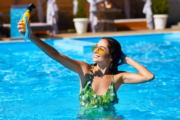 Жінка-блогер, яка фотографує селфі з камерою дій у басейні. Стиль життя відеоблогер фільмів з розкішного курорту в сонячний день. Гаряча дівчина в купальнику прямий ефір для соціальних медіа любить — стокове фото