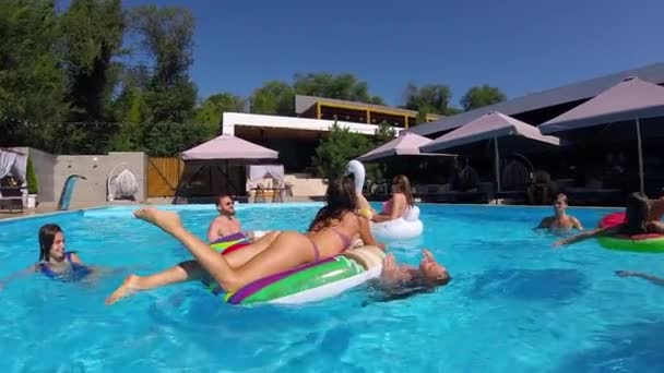 Amigos que se relajan en la piscina privada de la villa, mienten en el sol en el flamenco inflable, cisne, flotadores. Los jóvenes se relajan en la fiesta en el resort de lujo en un día soleado. Chicas de bikini tomando el sol. Movimiento lento. — Vídeo de stock