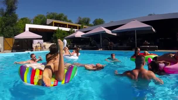 Amigos que se relajan en la piscina privada de la villa, mienten en el sol en el flamenco inflable, cisne, flotadores. Los jóvenes se relajan en la fiesta en el resort de lujo en un día soleado. Chicas de bikini tomando el sol. Movimiento lento. — Vídeos de Stock