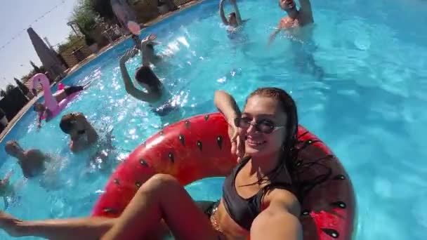 Lifestyle blogger woman taking selfie vídeo with action câmera floating on watermelon swim ring in pool. Viagem vlogger girl filmes vlog no resort. Festa de praia ao vivo feminina com amigos. Slomo. — Vídeo de Stock