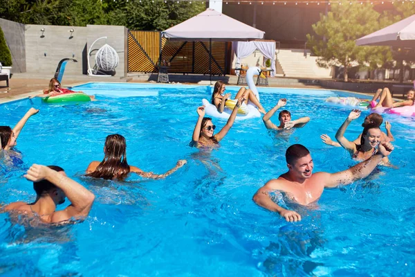 Grupo multirracial de amigos que fazem festa na piscina villa privada. Jovens felizes em roupa de banho dançando e salpicando com flutuações infláveis no resort de luxo no dia ensolarado. Meninas de biquíni. — Fotografia de Stock