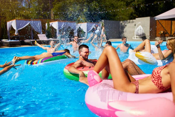 Amigos que fazem festa na piscina privada villa. Jovens felizes salpicando água e nadando no flamingo inflável, cisne, colchões no resort de luxo no dia ensolarado. Meninas de biquíni jazem ao sol . — Fotografia de Stock