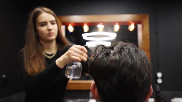 Peluquería rocía agua en el cabello del cliente antes de corte de pelo y peinado en la barbería. Peluquería mujer moja el cabello por aerosol y los peina en el salón de belleza. Master use la botella de rociador de agua en el estudio de belleza masculino . — Vídeos de Stock