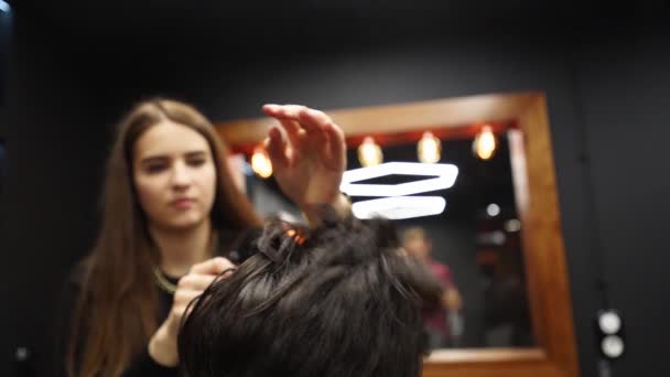 Barberaren sprayar vatten på klientens hår innan frisyr och styling i frisörsalongen. Frisör kvinna fuktar håret genom spray och kammar dem i frisör salong. Master använda vatten spruta flaska i manliga skönhet studio. — Stockvideo