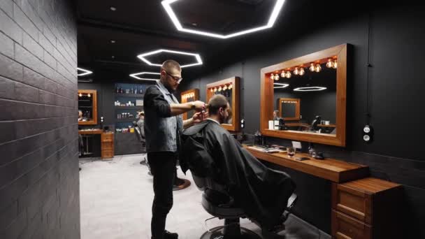 Trendy Friseur schneidet bärtige Männer Haare mit einem Clipper in Friseursalon. Herrenfrisur und Haarschnitt im Salon. Pflege der Haare mit Trimmer. Friseur beim Friseur im Retro-Friseursalon. Dolly in — Stockvideo