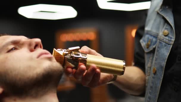 Peluquero en gafas corta la barba del hombre con un trimmer en la barbería. Peinado y corte de pelo en el salón. Arreglar el cabello con una podadora. Hipster peluquero haciendo corte de pelo en el salón de belleza retro . — Vídeos de Stock