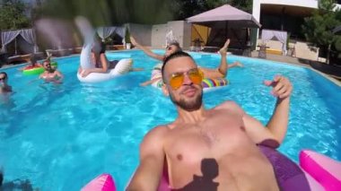 Yaşam stili blogcusu yüzme havuzunda kamerayla selfie çekiyor. Pembe flamingo üzerinde yüzen partilerin video günlükleri. Sosyal medya beğenileri için canlı yayın yapan uygun bir adam. Slomo