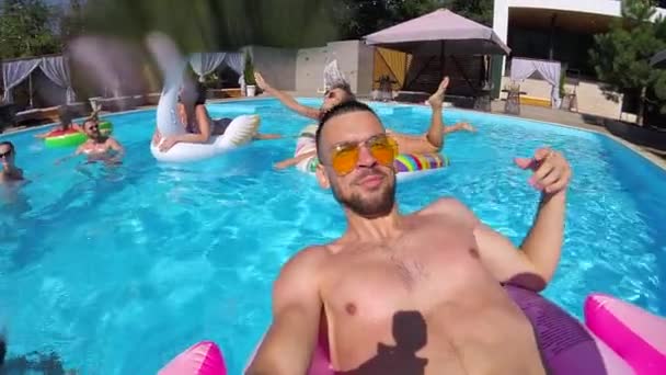 Bloger stylu życia robi selfie video z kamerą w basenie. Filmy vlogger podróży vlog z imprezy pływające na różowym flamingo. Dopasowany facet transmituje na żywo w mediach społecznościowych. Slomo. — Wideo stockowe