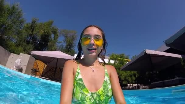 Mujer bonita equipada en traje de baño, gafas de sol buceando bajo el agua en la piscina, disparándose a sí misma en la cámara de acción. Chica de raza mixta filmando selfie video bañándose bajo el agua, relajándose en las vacaciones de verano — Vídeo de stock